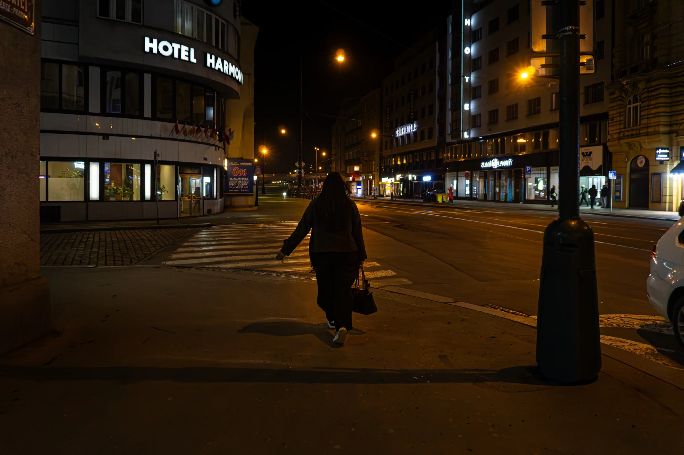 Een eenzame voetganger steekt bij nacht een verlicht kruispunt over