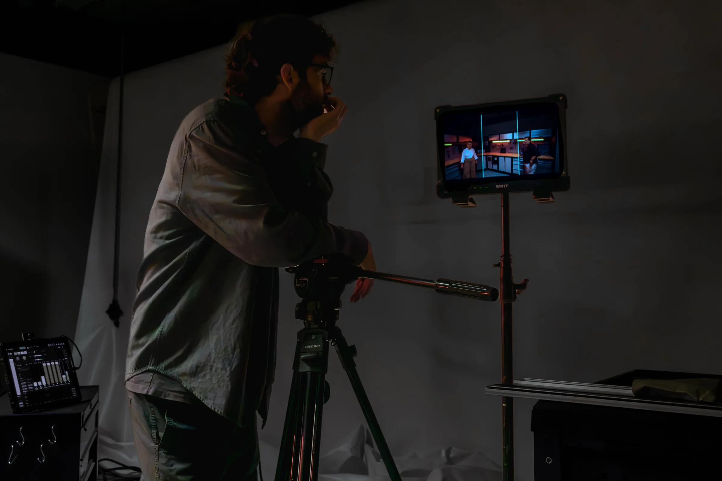 Een cameraman kijkt naar een monitor op een statief in een donkere studio