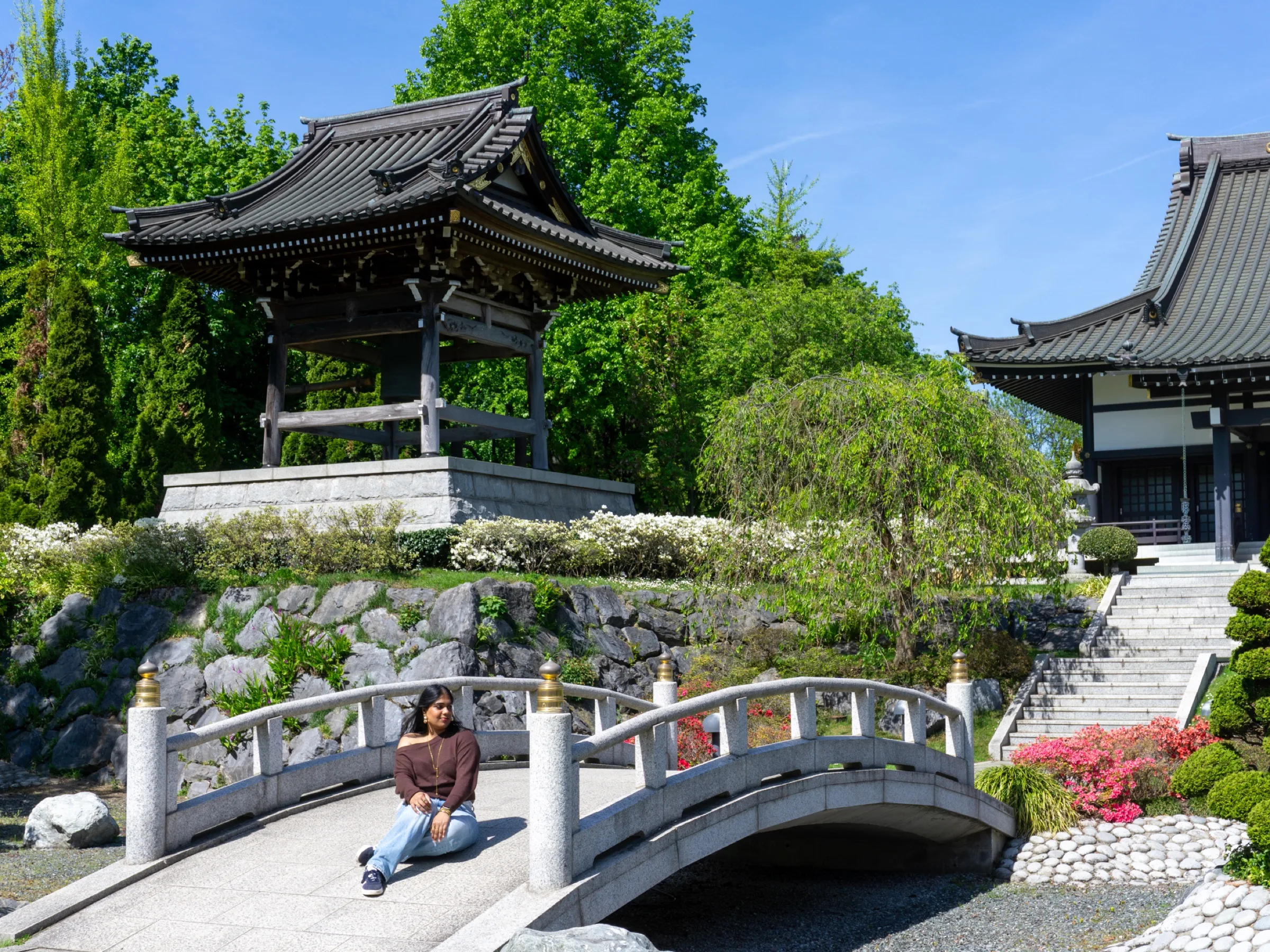 Een vrouw zit op een bruggetje onder een Japanse klokkentoren
