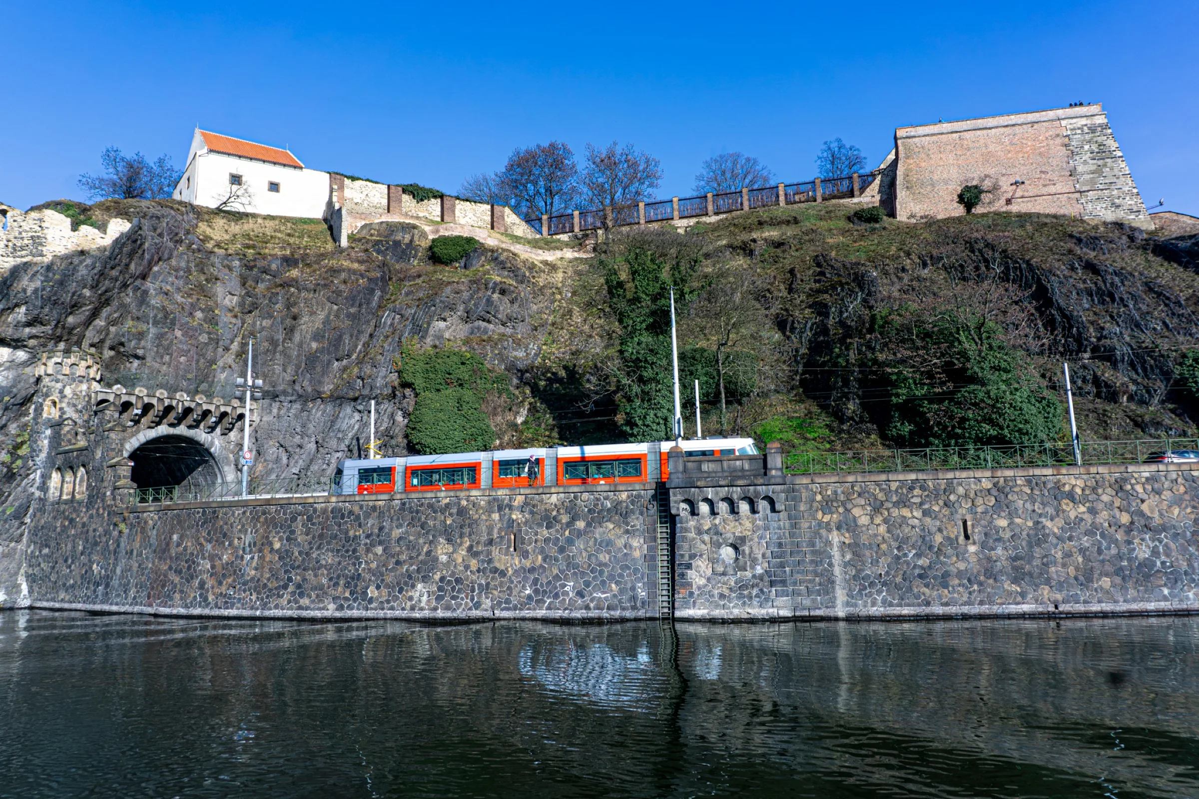 Een rotswand met huizen erboven en een trein langs het water