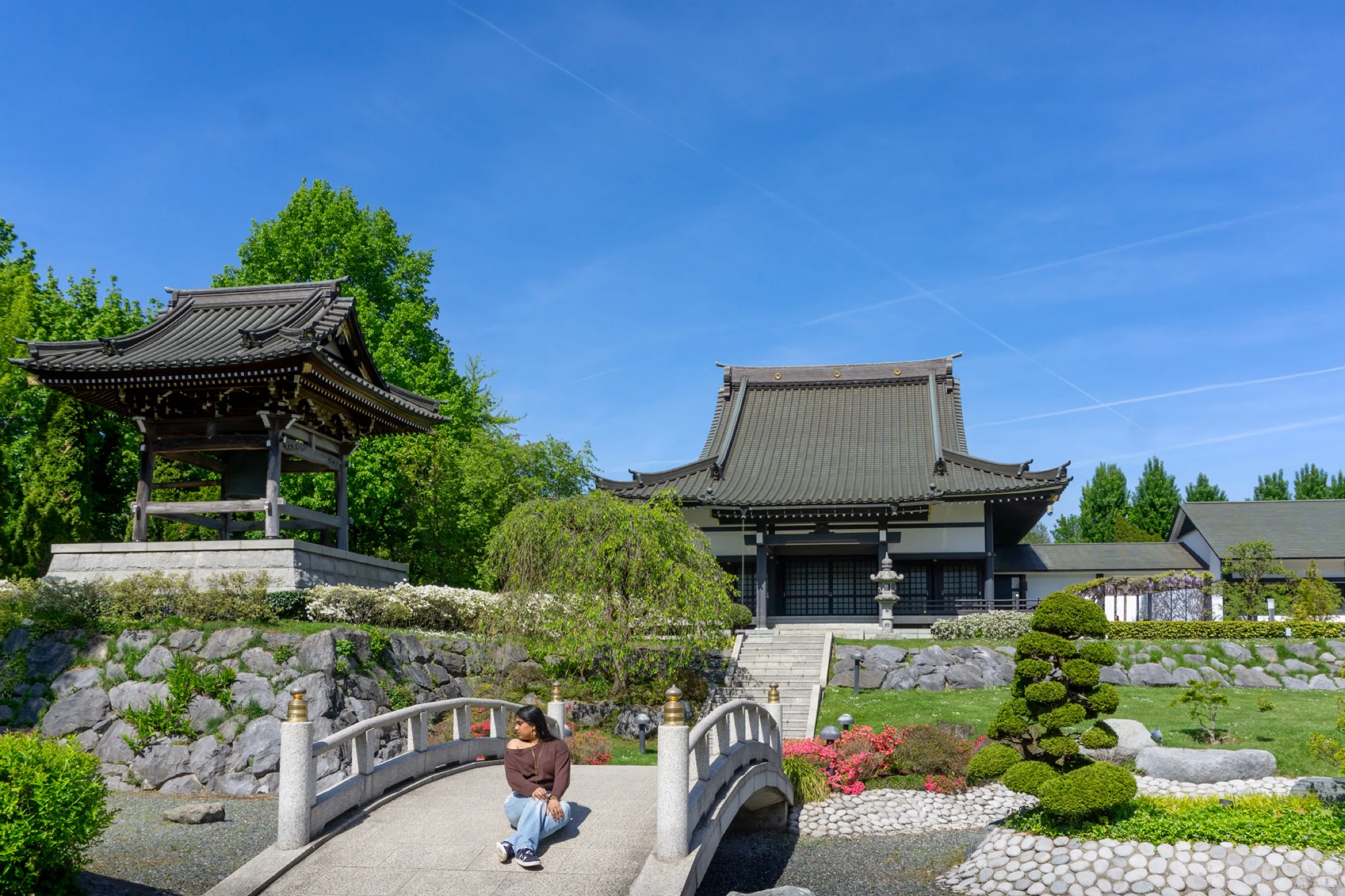 Een Japanse tempel en klokkentoren boven een tuin met een bruggetje