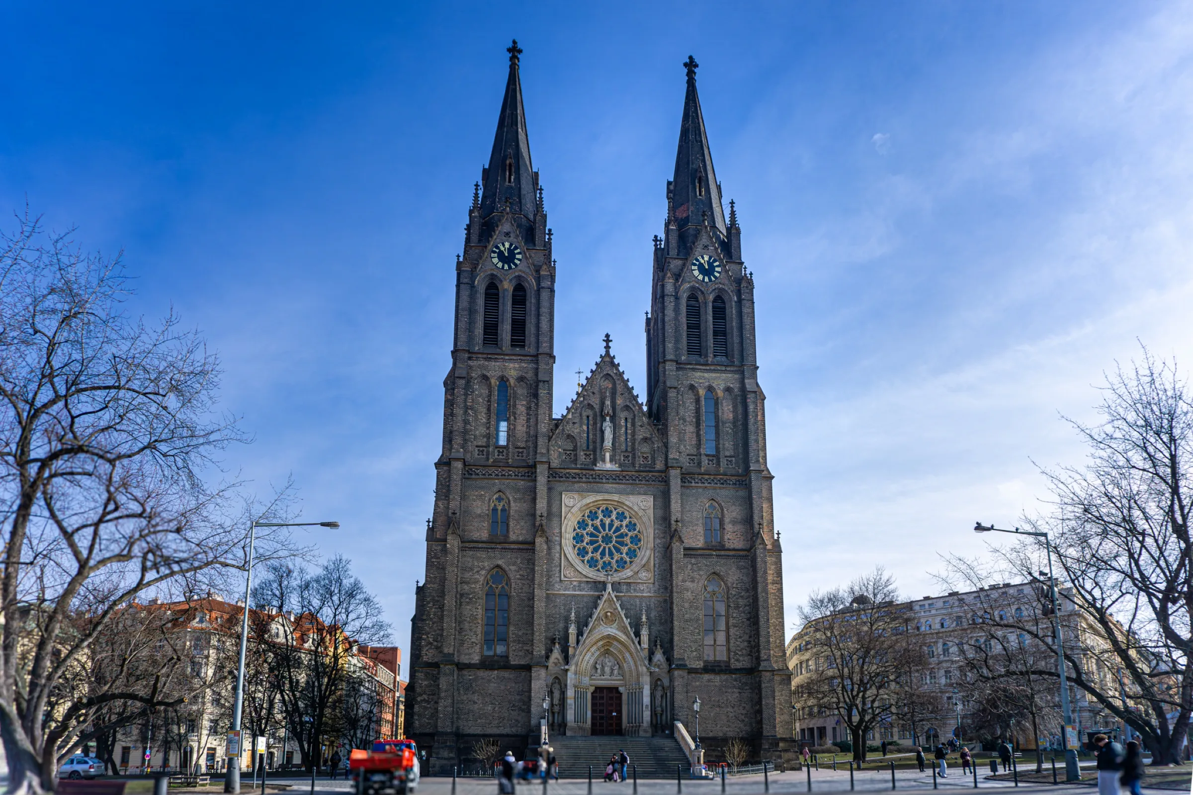 Een kerk met twee spitse torens aan een plein met kale bomen
