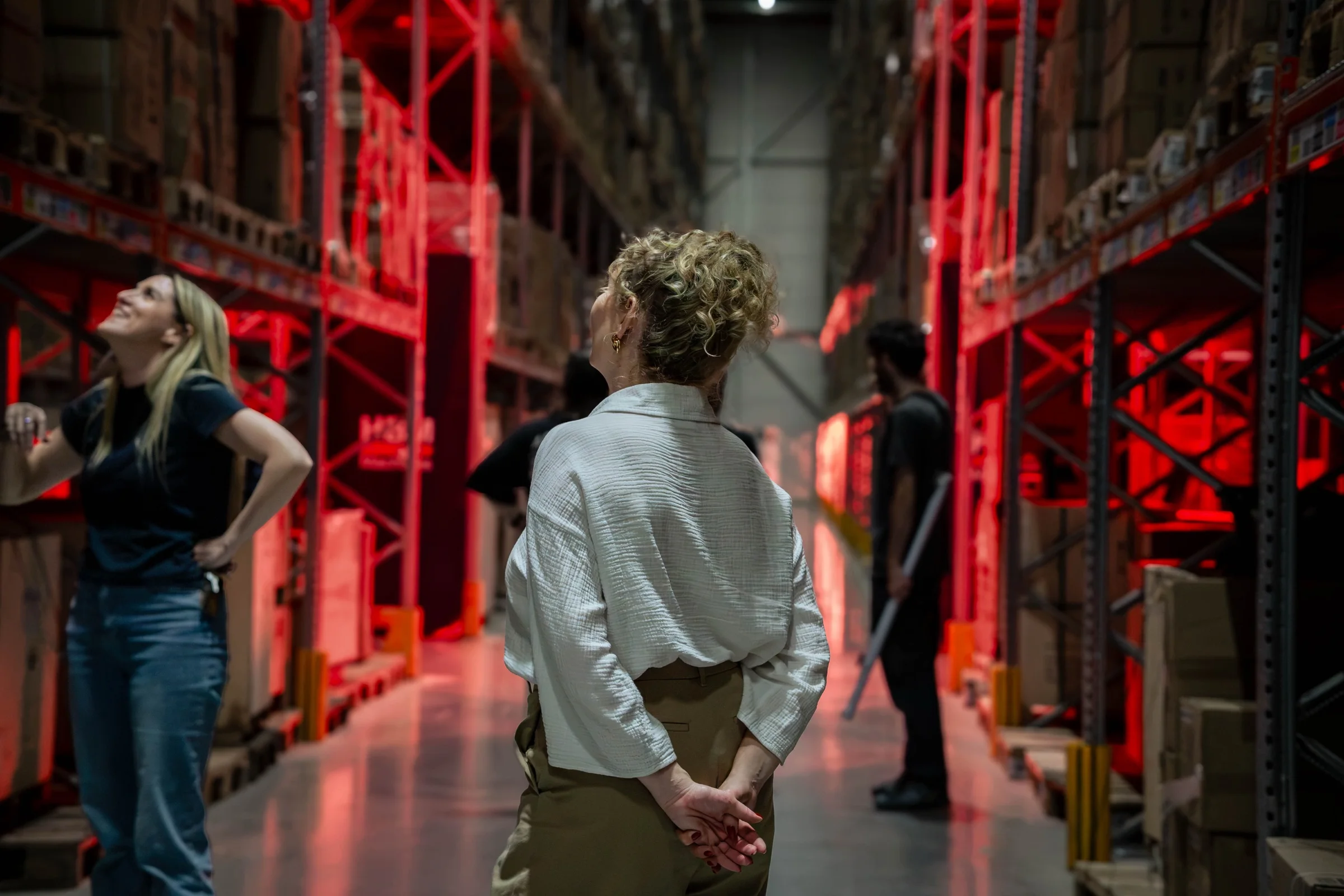 Twee vrouwen in een magazijn vol rood verlichte stellingen tijdens een videoshoot