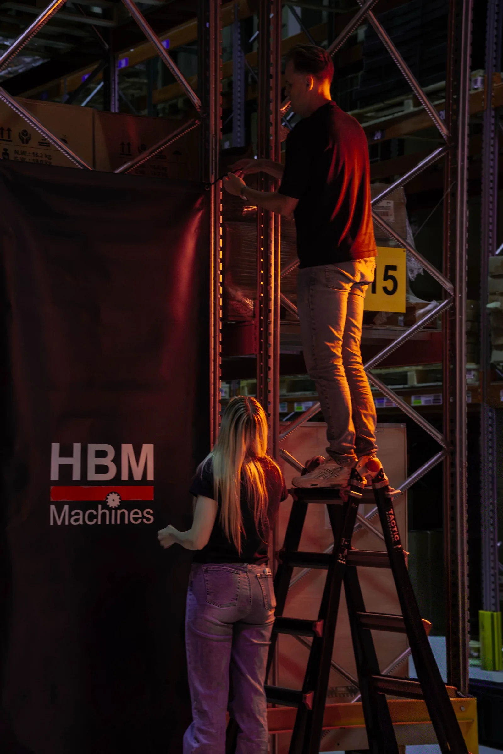 Een man op een ladder hangt een HBM-doek op, een vrouw kijkt toe