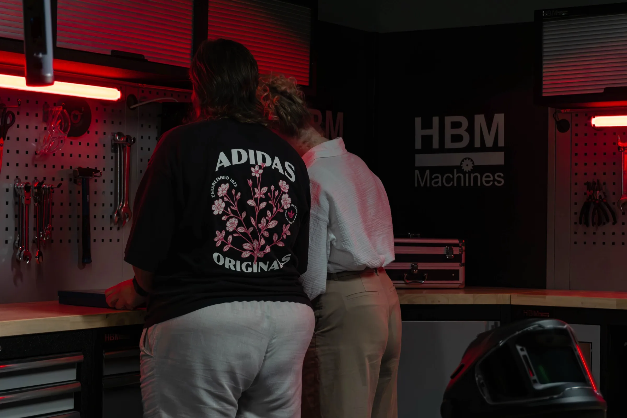 Twee mensen bij een werkbank onder rood licht, een HBM-logo aan de muur